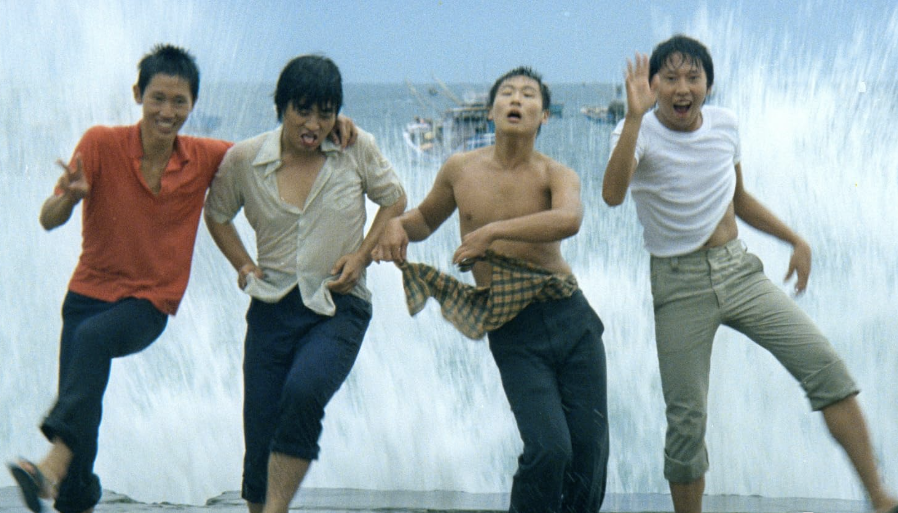 Four young men dancing with the ocean splashing behind them.